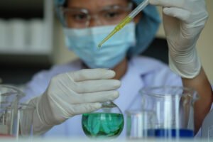 Masked laboratory technician using a pipette to transfer chemical solution into a flask