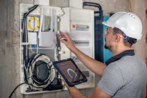 Electrical technician inspecting an electrical control panel using a digital testing device